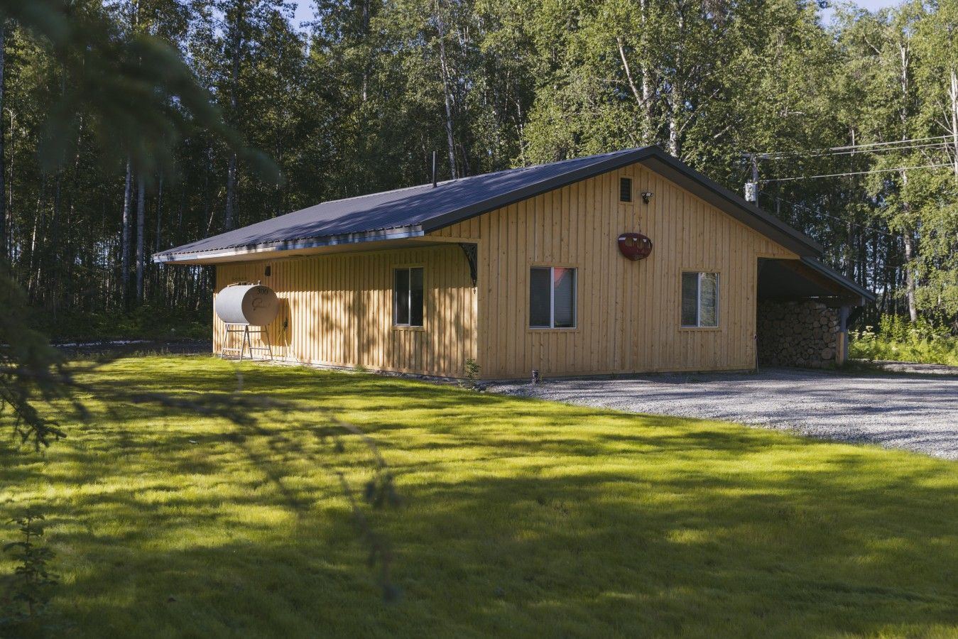 A wooden cabin with a gravel driveway, a small attached garage, and a stone wall.