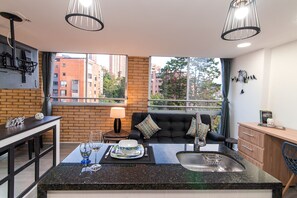 A modern kitchen with a dining area, large windows, and a view of buildings. - Staynova Acogedor Loft en El poblado (Medellín)