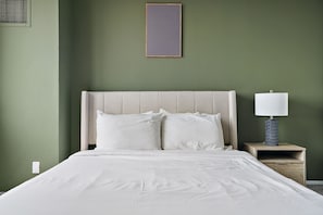 Una cama bien hecha con sábanas blancas, un cabecero y una mesita de noche con una lámpara.