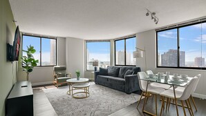 A modern living room with a gray sofa, a glass dining table, and a large window offering a city view.