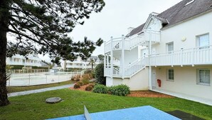 Un edificio blanco con balcón, una zona de juegos azul y un césped bien cuidado.