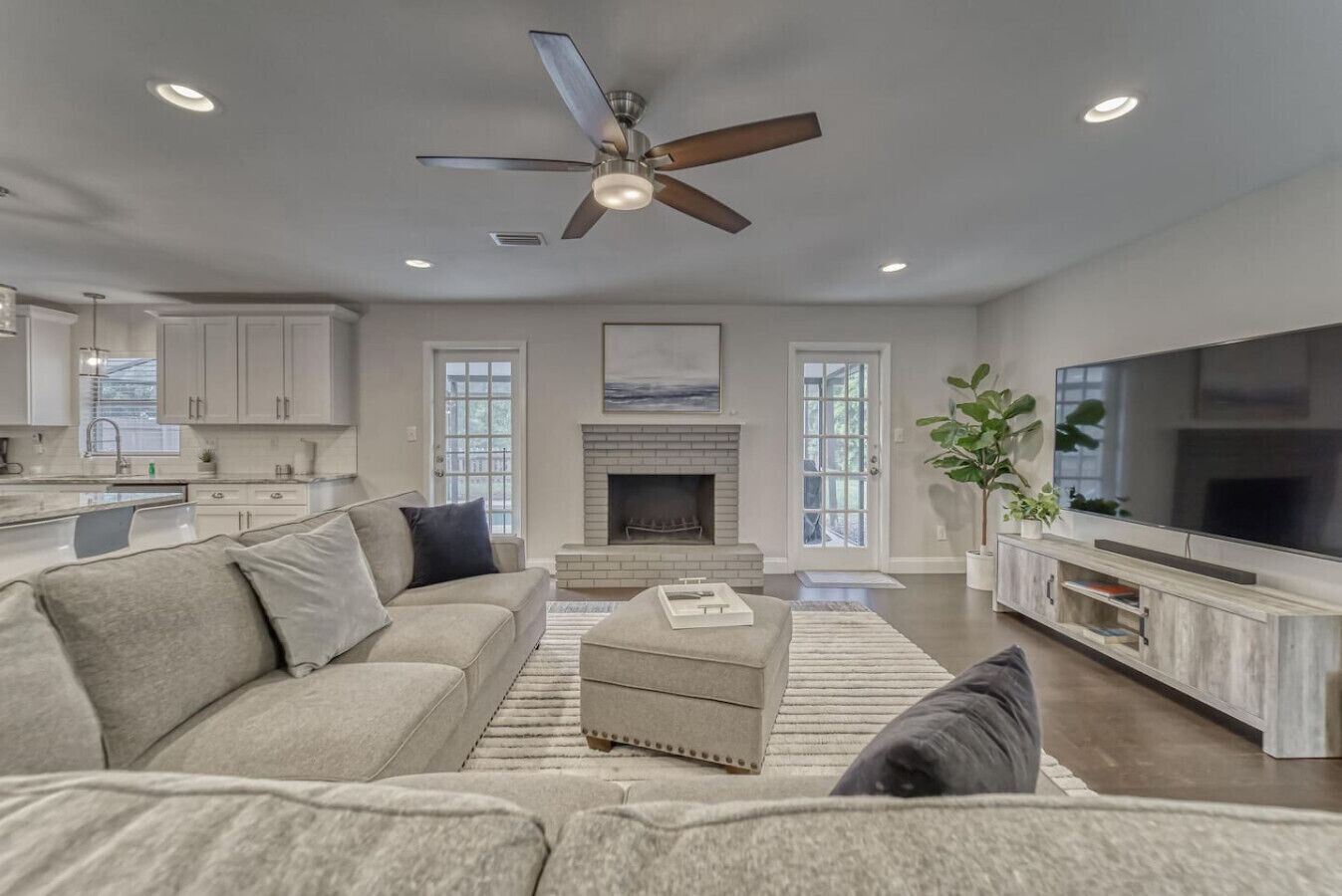 A modern living room with a sofa, ottoman, fireplace, television, and ceiling fan.