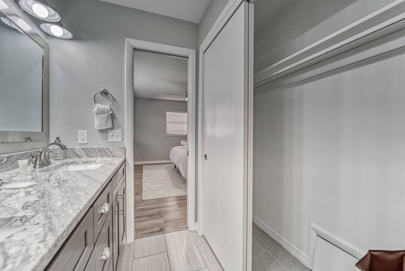 A modern bathroom with a marble countertop, a sink, and a mirror. There is a towel rack and a door leading to another room.