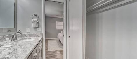 A modern bathroom with a marble countertop, a sink, and a mirror. There is a towel rack and a door leading to another room.