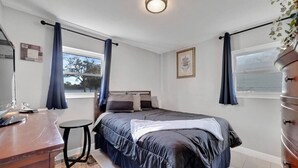 Un dormitorio con cama, escritorio, silla, cómoda y ventana con cortinas.