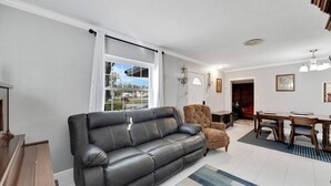 Una sala moderna con un sofá de cuero, un sillón estampado y un comedor con muebles de madera.