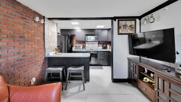 Un espacio habitable pequeño con cocina, comedor para dos con dos taburetes, televisor y sillón de cuero.