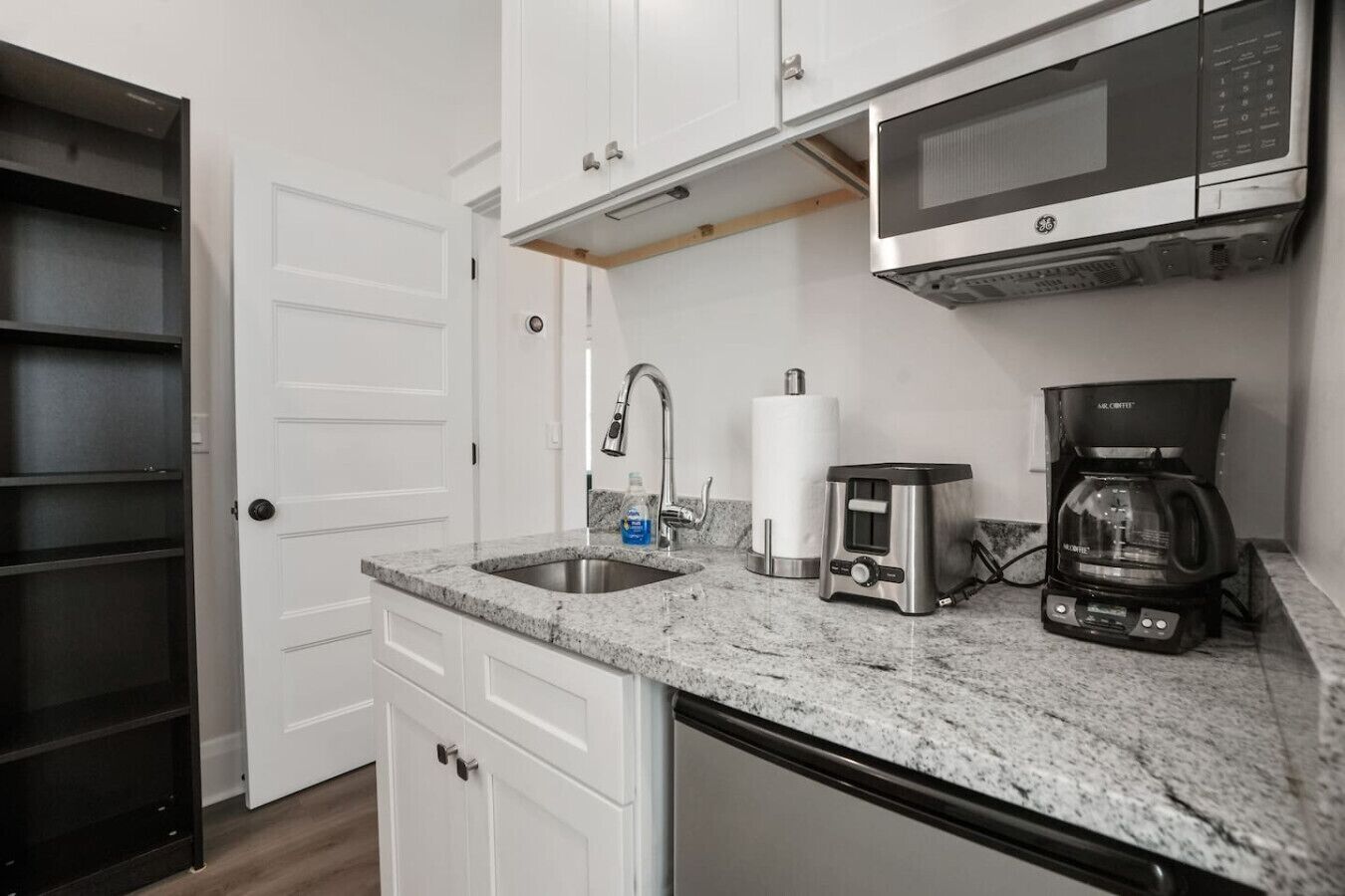 Una cocina compacta con microondas integrado, cafetera y lavamanos con grifo.