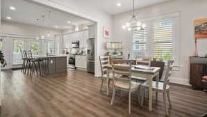 Una cocina moderna con armarios blancos, electrodomésticos de acero inoxidable y un comedor con sillas y mesa de madera.