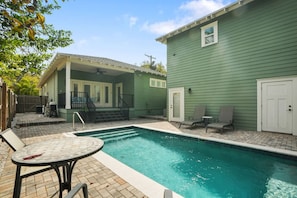 A backyard with a swimming pool, a covered patio, and a green house.