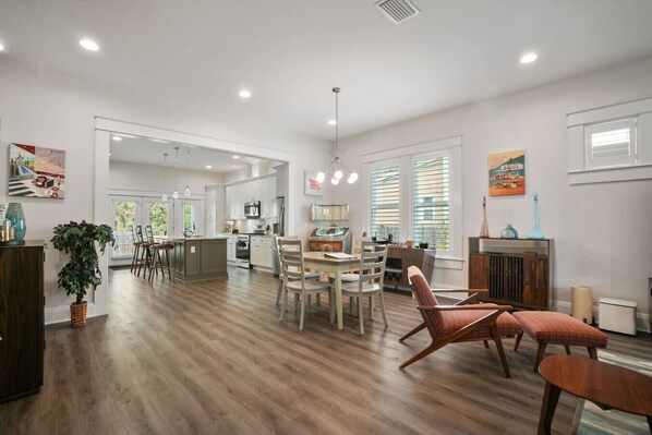 A spacious living area with a wooden floor, a dining table, and a kitchen in the background.