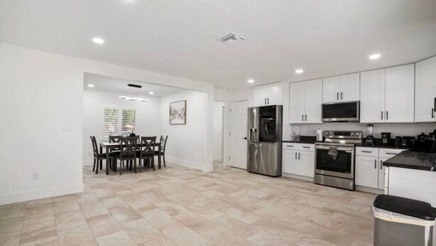 A modern kitchen with white cabinets, stainless steel appliances, and a dining area with a table and chairs. - Expansive Charm - 4BR Estate on Private Acre (Brandon)