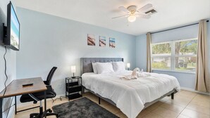 A hotel room with a bed, a desk with a chair, a TV, and a ceiling fan. - King-Style Retreat · 4 BR · Family Friendly (Tampa)