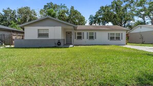 A single-story house with a front porch, a small attached garage, and a well-maintained lawn. - King-Style Retreat · 4 BR · Family Friendly (Tampa)