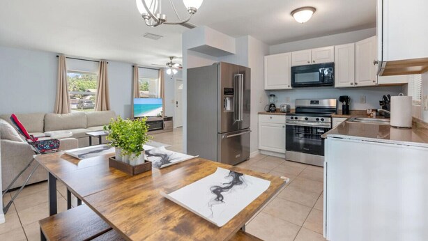 A modern kitchen with stainless steel appliances, a dining area with a wooden table, and a living room with a sofa and TV. - King-Style Retreat · 4 BR · Family Friendly (Tampa)