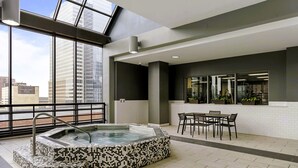 Een dakterras met een hottub, eethoek en grote ramen met uitzicht over de stad.