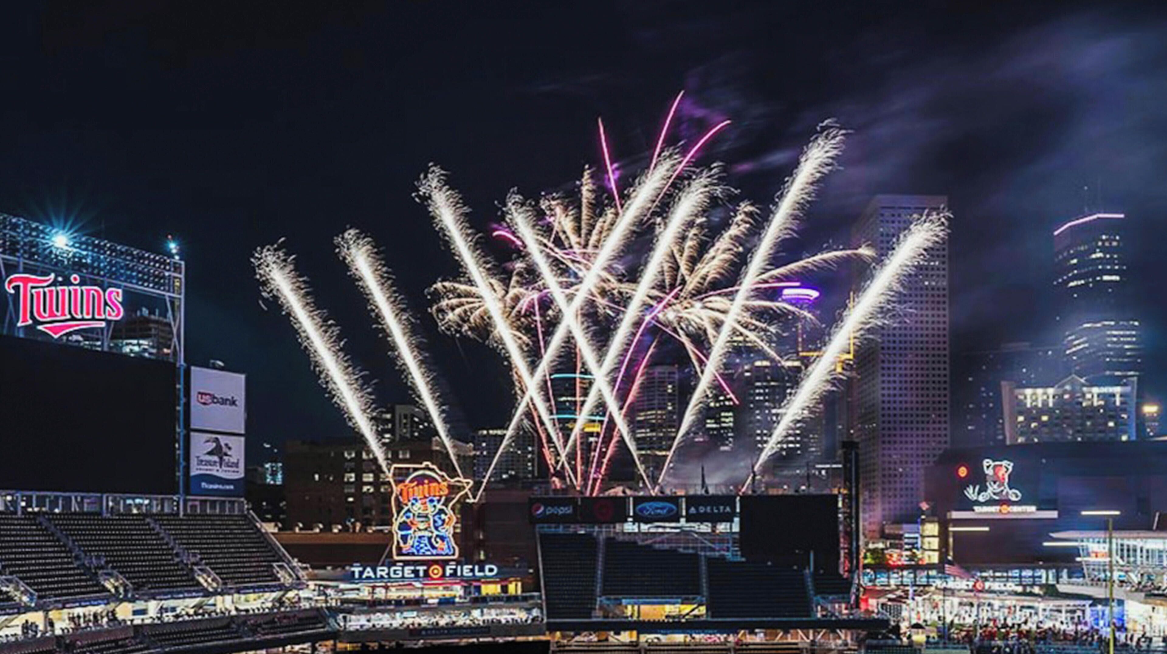 A nighttime view of a stadium with fireworks display, Target Field, and surrounding cityscape.