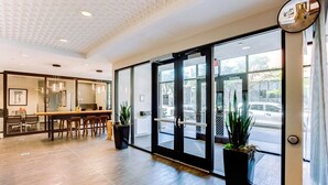 Een moderne hotel lobby met een receptiebalie, een zithoek en grote glazen deuren die uitkomen op de straat.