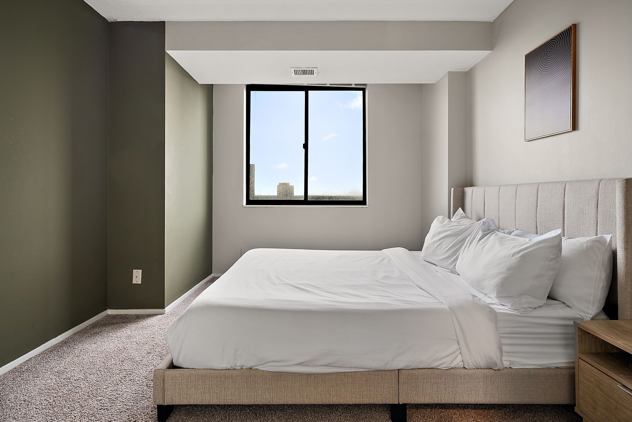A bedroom with a large window, a bed, a nightstand, and a headboard.