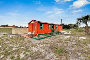 A small, single-story red house with a porch and outdoor seating.