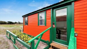 Un edificio rojo con detalles en verde y una puerta, rodeado de césped, una banca y plantas.
