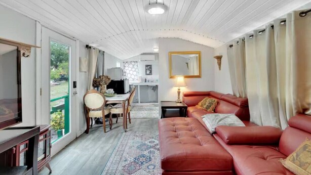 Una sala de estar acogedora con un sofá rojo, una mesa de comedor con sillas, un televisor y una cocina al fondo.