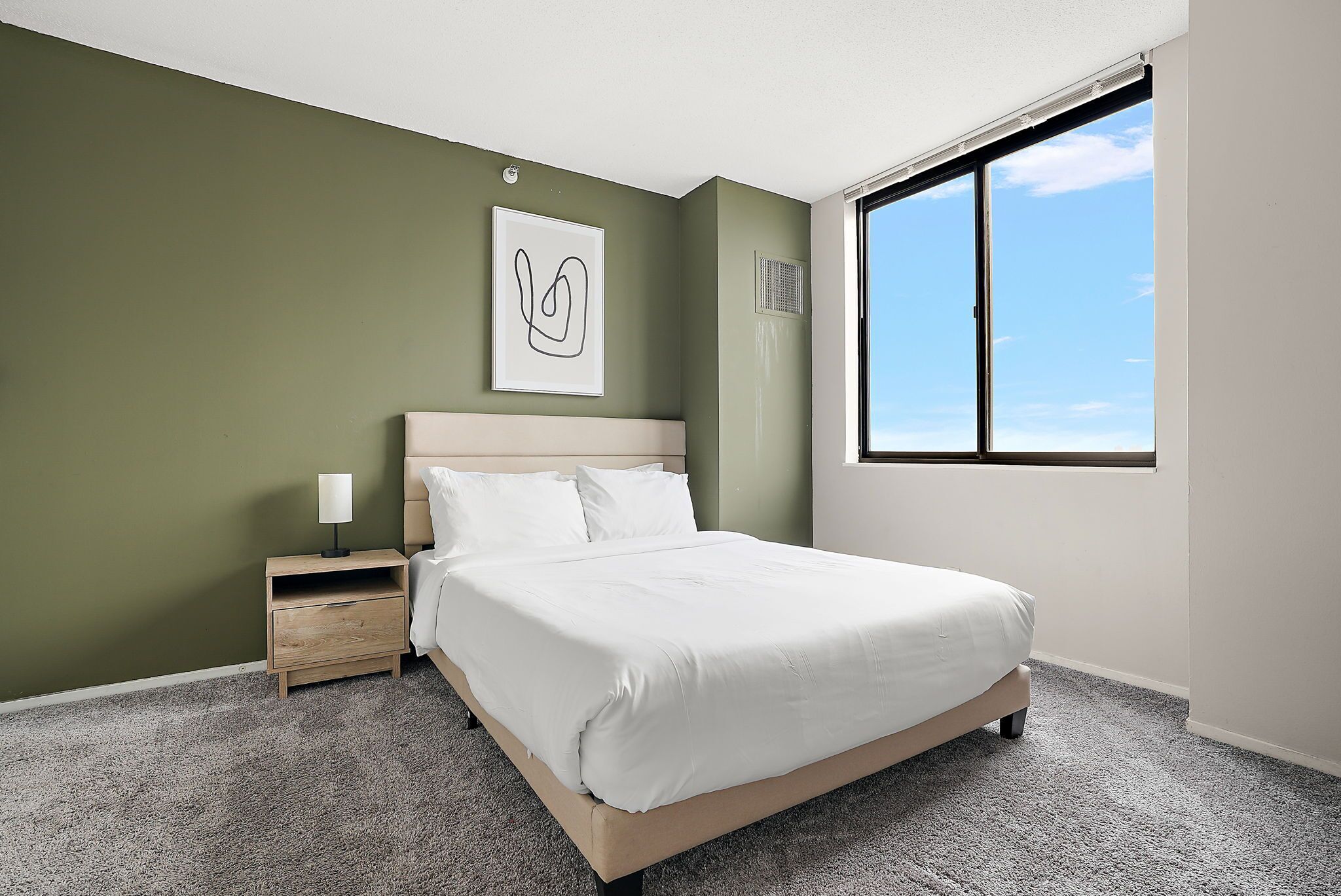 A bedroom with a bed, nightstand, and a window with a view of the sky.