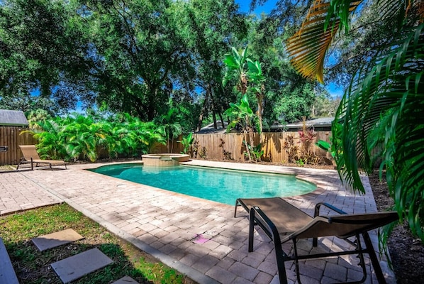 Un jardin à l’arrière de la maison, avec une piscine, entouré d’une clôture en bois et d’une végétation luxuriante.