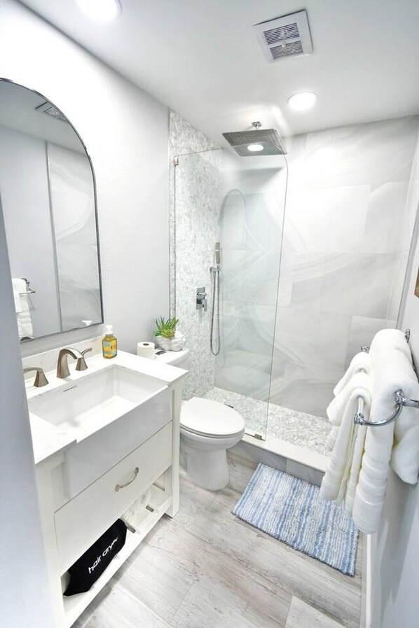 A modern bathroom with a glass-enclosed shower, a white sink, and a toilet.