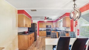 Une cuisine moderne avec des meubles en bois, un coin repas avec des chaises noires et un ventilateur de plafond.