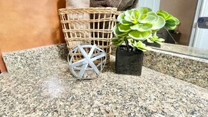 Un bagno con un piano di lavoro in granito, un cesto in vimini con asciugamani, una succulenta in vaso e una sfera decorativa in metallo.