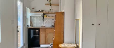 A compact bedroom with a bed, a bedside table, and a view of a kitchen with a refrigerator and wooden cabinets.