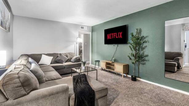 A modern living room with a sectional sofa, a coffee table, a TV mounted on a green wall, and a sideboard.