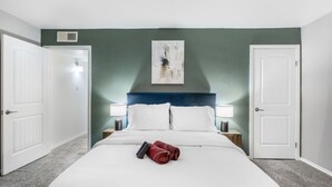 A hotel room with a bed, two bedside tables with lamps, a painting on the wall, and two doors.