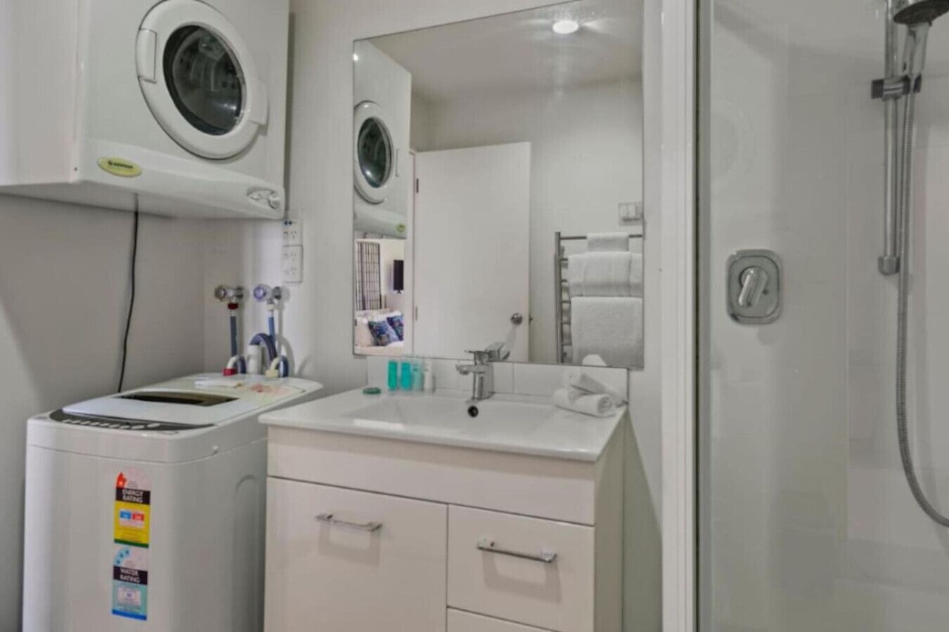 Ein Badezimmer mit Waschmaschine, Waschbecken, Spiegel und Dusche.