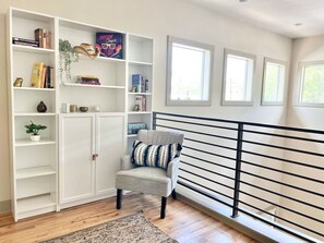 A room with a white bookshelf, a grey armchair with a striped pillow, and a black railing. - Walk to UT & Moody Center. Spacious & Cozy Retreat (Austin)