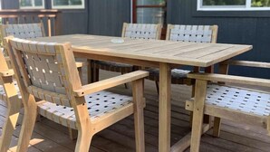 Une terrasse en bois avec une table et des chaises, des unités de climatisation fixées au mur et des fenêtres.