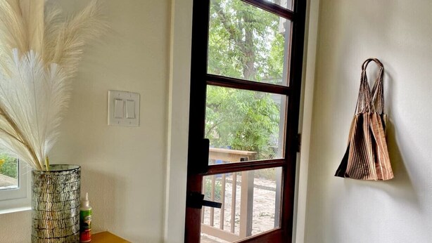 Une pièce avec une table en bois, un vase contenant des plantes séchées, une porte donnant sur l’extérieur et un sac fixé au mur.