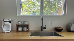 Une cuisine dotée d’un plan de travail en bois, d’un évier en acier inoxydable, d’une machine à café, d’un grille-pain et d’une fenêtre donnant sur les arbres.