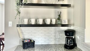 A kitchen with white hexagonal tiles, a coffee maker, and a shelf with white cups and a plant. - The Lovely. Perfect ATX Family Getaway (Austin)