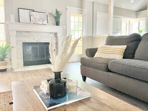 A living room with a fireplace, a grey sofa, and a coffee table with books and a vase. - The Lovely. Perfect ATX Family Getaway (Austin)