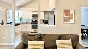 A modern kitchen with white cabinets, stainless steel appliances, and a dining area with a table and chairs. - The Lovely. Perfect ATX Family Getaway (Austin)