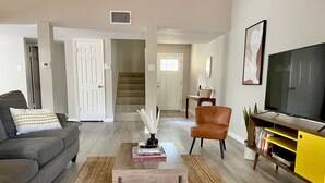 A living room with a sofa, coffee table, armchair, TV stand, and staircase leading to another room. - The Lovely. Perfect ATX Family Getaway (Austin)