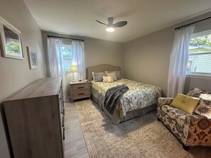 Ein Schlafzimmer mit Bett, Nachttisch, Schminktisch und Deckenventilator.