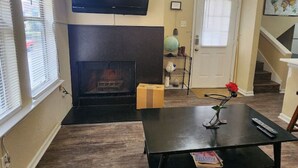 A living room with a fireplace, a flat-screen TV mounted above it, and a coffee table with a vase and remote controls. - Lovely South Austin Condo. All Essentials Included (Austin)