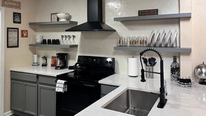 A modern kitchen with grey cabinets, a black stove, and stainless steel appliances. There are shelves with dishes and a sign indicating kitchen help wanted. - Lovely South Austin Condo. All Essentials Included (Austin)