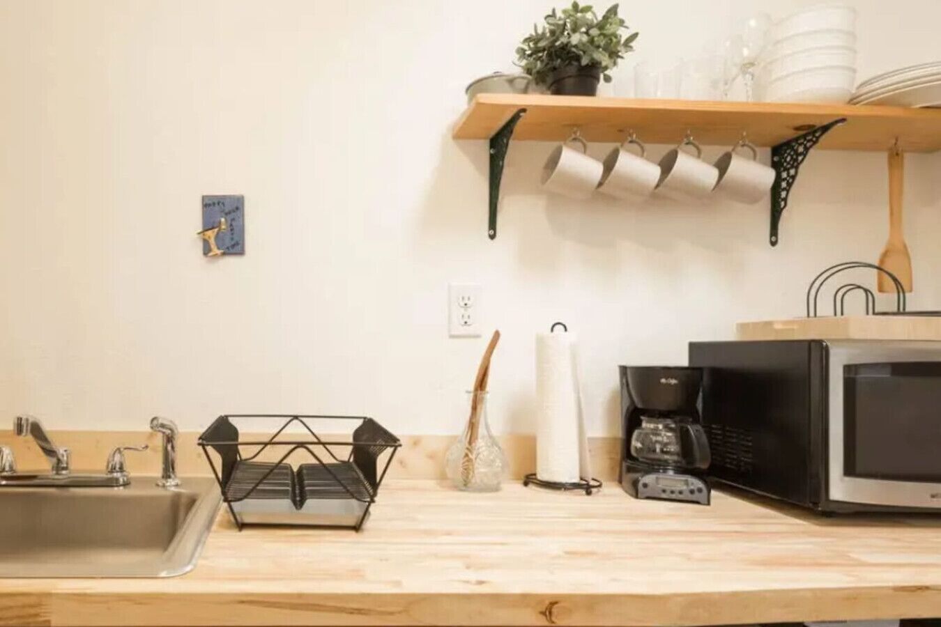 Een keuken met een houten aanrecht, een spoelbak, een koffiezetapparaat, een magnetron en een hangende panrek.