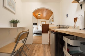 A compact kitchen with wooden flooring, a dining area with a chair, and a small table.