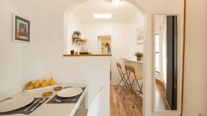 A compact dining area with a white table set for four, a small kitchen in the background, and a mirror on the right. - East Austin Garden Cottage |  Sweet & Private (Austin)