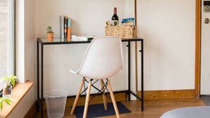 A modern room with a flat-screen TV mounted on the wall, a small desk with a chair, a wicker basket, and a potted plant. - East Austin Garden Cottage |  Sweet & Private (Austin)